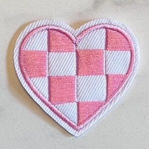 May include: Embroidered heart patch with a pink and white checkered pattern. The patch has a white border and a pink outline. The heart shape is a classic symbol of love and affection, perfect for adding a touch of charm to clothing or accessories.