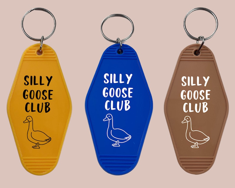 Peut inclure: Trois porte-cl&eacute;s en forme de cl&eacute;s de chambre d'h&ocirc;tel avec le texte "Silly Goose Club" et une illustration de canard de dessin anim&eacute;. Les porte-cl&eacute;s sont jaunes, bleus et bruns.
