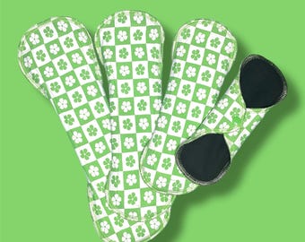 May include: A set of four reusable cloth pads with a green and white checkered pattern featuring small white flowers. The pads are made of soft, absorbent fabric and are designed to be comfortable and discreet.