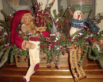 May include: A rustic Christmas centerpiece featuring a handmade Santa and snowman doll, surrounded by greenery, red berries, and a wooden tag that reads "Christmas Blessings".