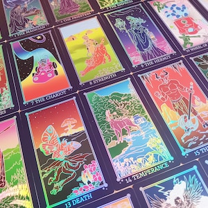 Op de afbeelding: Een verzameling tarotkaarten met levendige illustraties en holografische accenten. Elke kaart heeft unieke kunstwerken, waaronder figuren, symbolen en tekst. De kaarten zijn in een raster gerangschikt en tonen de diverse thema's van het deck.