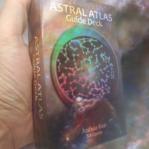 May include: A rectangular deck of cards box titled Pandemonia Astral Atlas Guide Deck by Joshua Kes. The box features a colorful nebula background with a circular graphic containing white constellation patterns and the text 54 Cards on the front.