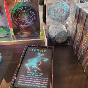 The Astral Atlas Guide Deck box and cards on display on a shelf at a trade show.