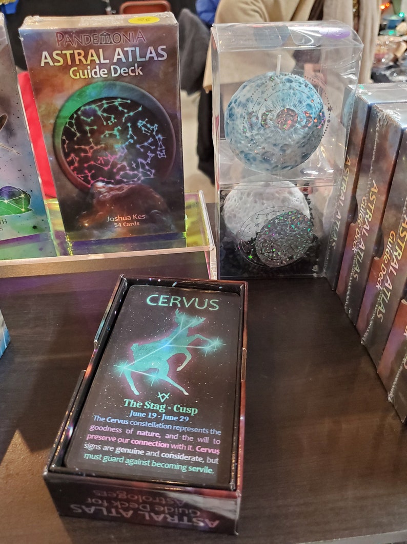 The Astral Atlas Guide Deck box and cards on display on a shelf at a trade show.