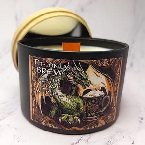 May include: A black candle jar with a green dragon holding a beer mug. The jar has a label that reads "The Only Brew For the Brave & True."