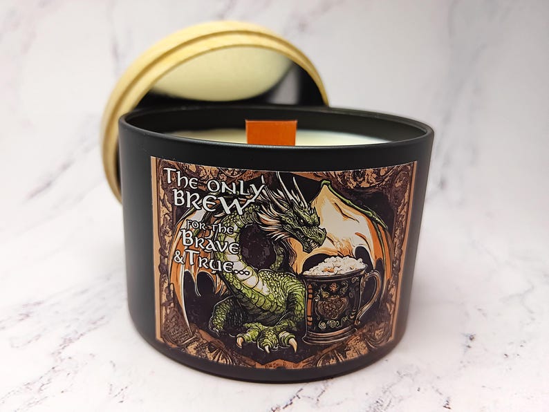May include: A black candle jar with a green dragon holding a beer mug. The jar has a label that reads "The Only Brew For the Brave & True."