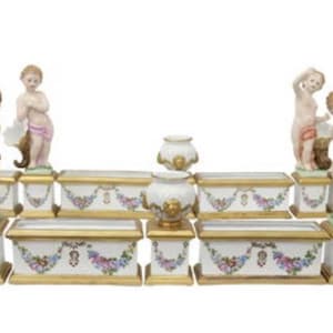 Puede incluir: Un centro de mesa de porcelana blanca en forma de fuente con figuras de querubines, detalles dorados y florales. La fuente está compuesta por varias secciones que se pueden organizar de diferentes maneras.