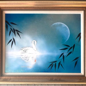 May include: A framed painting depicts a white swan on a reflective surface under a blue moon. Dark bamboo leaves frame the scene, set against a gradient blue sky. The artwork is encased in a gold-toned frame.