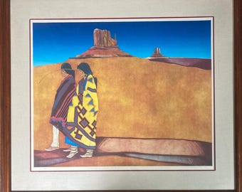 May include: A framed print of a painting depicting two Native American figures in traditional clothing walking in a desert landscape with a red rock formation in the background.