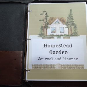 Könnte beinhalten: Ein Ordner mit einem grünen und braunen Einband, der eine Aquarell-Illustration eines weißen Hauses mit braunem Dach und zwei grünen Bäumen zeigt. Der Text "Homestead Garden Journal and Planner" ist in Schwarz auf dem Einband gedruckt.