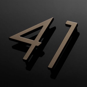 May include: A close-up of a house number sign with the number 41 in a modern, minimalist style. The number is made of a metallic material with a brushed finish, giving it a sleek and contemporary look.