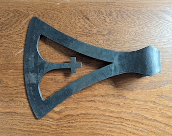 Peut inclure: Une tête de hache en métal noir avec un motif en forme de croix au centre. La tête de hache est en forme de triangle avec un bord incurvé.