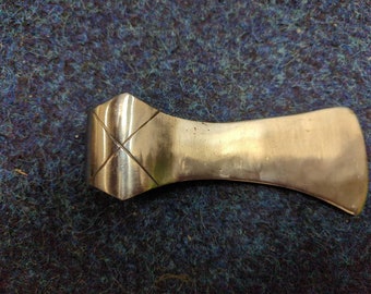 May include: A silver axe head with a diamond-shaped pattern on the top. The axe head is smooth and polished.