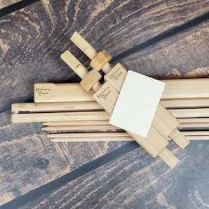 May include: Two wooden clamps with the text "Haftowany Zakątek" engraved on them. The clamps are used to hold wooden dowels together. The dowels are 50 cm long and made in Poland.