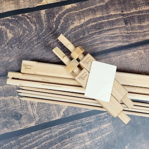 Op de afbeelding: Een set houten pinnen en twee houten klemmen met de tekst "Harmoniczny Zasiek" erop. De pinnen zijn 80 cm lang en gemaakt in Polen.