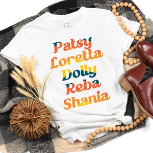 May include: White t-shirt with the names "Patsy", "Loretta", "Dolly", "Reba", and "Shania" printed in a colorful retro font.