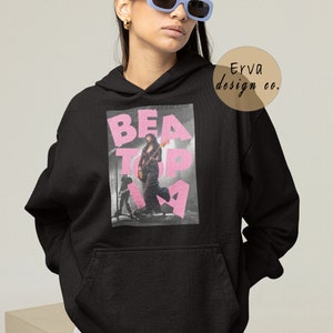 May include: Black hooded sweatshirt with a pink graphic print of a woman playing a guitar on stage. The graphic text reads "BEATopia".
