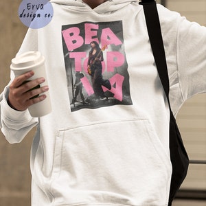 May include: White hoodie with a pink graphic print of a woman playing a guitar with the text "BEATOPIA".