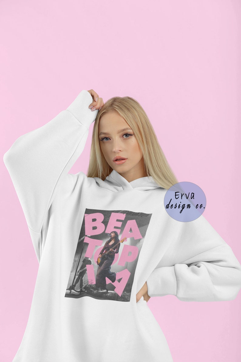 May include: White oversized hoodie with a pink graphic print of a woman playing a guitar with the text "BEAT TOPIA". The hoodie has a drawstring hood and kangaroo pocket.