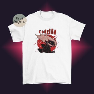 Könnte beinhalten: Weißes T-Shirt mit einer schwarzen und roten Illustration von Godzilla mit dem Wort "godzilla" in rot über der Illustration.