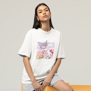 May include: A white t-shirt with a graphic print of two cartoon characters. The characters are a purple and pink cat with a pink bow and a white cat with a pink bow. The text "Doki" is printed below the characters.
