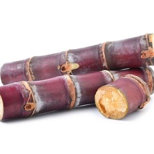 May include: Three segments of dark purple sugarcane stalks with visible nodes and fibrous, light-colored interiors. The cylindrical pieces are arranged in a stack, showcasing the deep reddish-purple outer skin and the woody, textured ends.