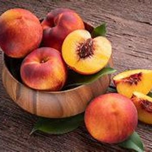 May include: A wooden bowl filled with ripe peaches, some sliced in half, with green leaves scattered around the bowl.