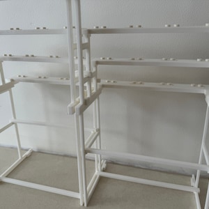 May include: White plastic shelf unit with multiple shelves. The shelves are made of a grid pattern and are designed to hold small items.