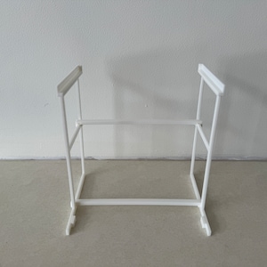 May include: White plastic shelf organizer with two levels. The shelf is made of a simple, rectangular design with a white finish.