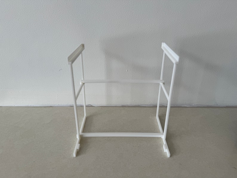 May include: White plastic shelf organizer with two levels. The shelf is made of a simple, rectangular design with a white finish.
