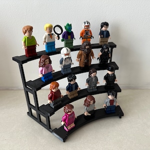 May include: A black tiered display stand with 15 miniature figurines. The figurines are made of plastic and are in various colors, including green, blue, red, brown, and black. The figurines are arranged in rows on the stand, with the top row having the most figurines.