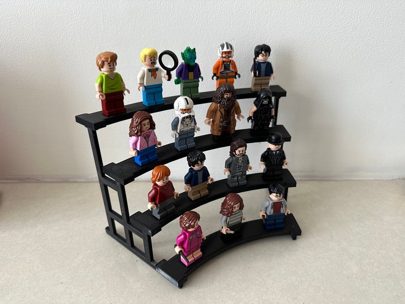 May include: A black tiered display stand with 15 miniature figurines. The figurines are made of plastic and are in various colors, including green, blue, red, brown, and black. The figurines are arranged in rows on the stand, with the top row having the most figurines.