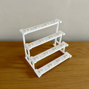 May include: White plastic Lego brick storage stand with four shelves. Each shelf has multiple holes for storing Lego bricks.