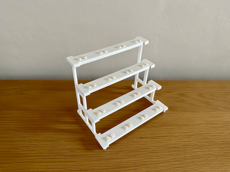 May include: White plastic Lego brick storage stand with four shelves. Each shelf has multiple holes for storing Lego bricks.