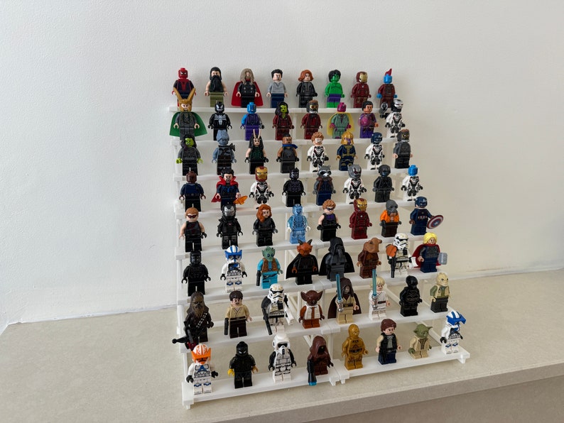 May include: A white tiered display shelf with a collection of miniature Lego minifigures. The figures are arranged in rows and include characters from Marvel and Star Wars.