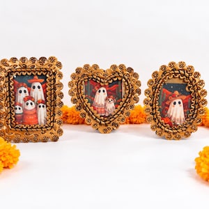 May include: Three decorative frames with textured gold borders. The rectangular frame shows a group of ghosts, the heart-shaped frame shows ghosts with a dog, and the oval frame shows a single ghost wearing a sombrero, all against red backgrounds.