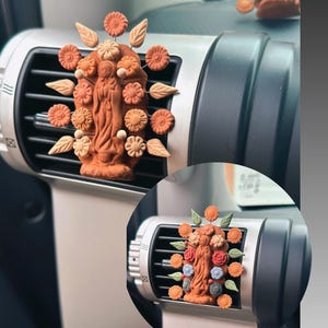 May include: A terracotta figurine of the Virgin Mary surrounded by colorful flowers, attached to a car's air vent.