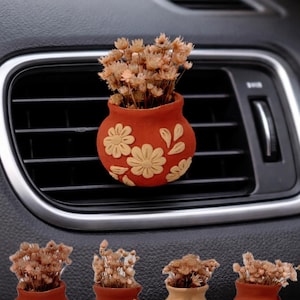 May include: A terracotta-colored car air vent diffuser shaped like a small vase, filled with dried flowers. The vase is decorated with cream-colored floral designs. Four additional vases are displayed below, labeled A, B, C, and D.
