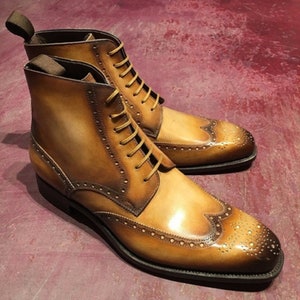 May include: Tan leather lace-up boots with a wingtip design and a brogue pattern. The boots have a pointed toe and a low heel.
