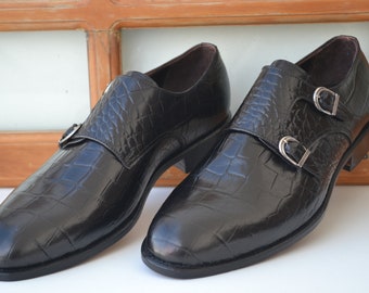 May include: A pair of black leather dress shoes with double buckles. The shoes have a crocodile-embossed pattern.
