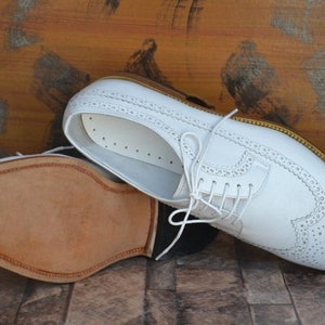 May include: White leather brogue shoes with a lace-up closure and a perforated design. The shoes have a brown leather sole.