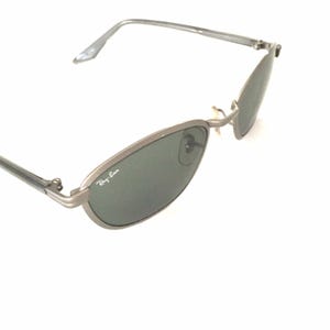 May include: Silver Ray-Ban sunglasses with green lenses. The sunglasses have a thin metal frame and a classic oval shape.