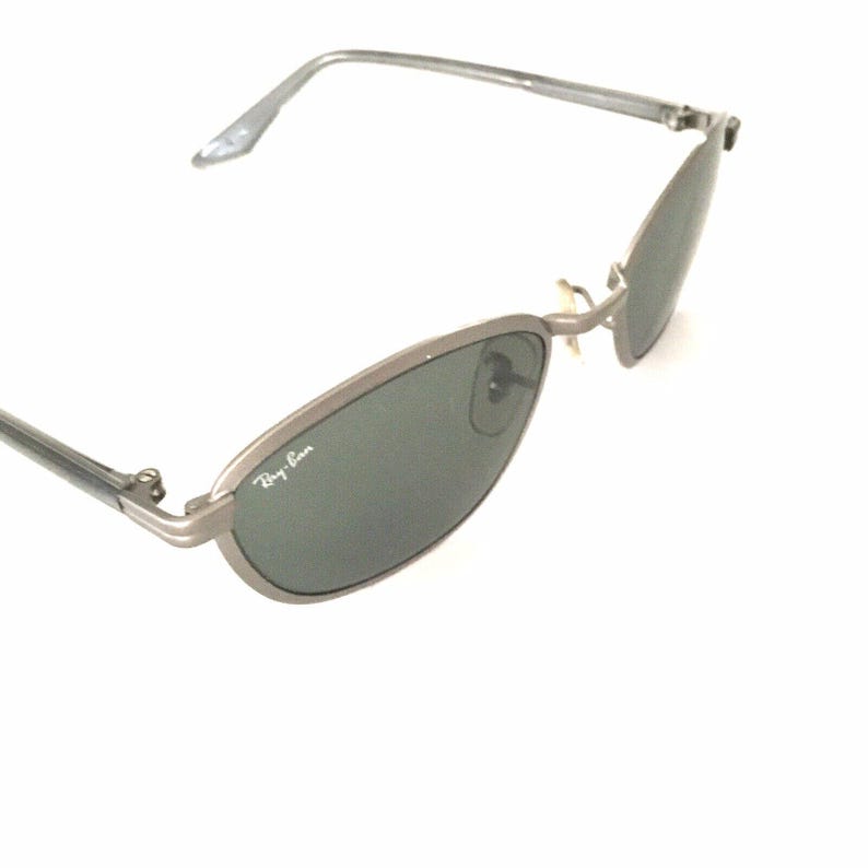 May include: Silver Ray-Ban sunglasses with green lenses. The sunglasses have a thin metal frame and a classic oval shape.
