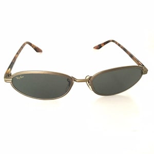 Puede incluir: Gafas de sol ovaladas con montura color bronce y lentes oscuras. Las patillas presentan un dise&ntilde;o de carey. El logotipo de Ray-Ban es visible en la lente izquierda. Un accesorio de gafas cl&aacute;sico.