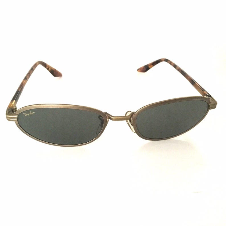 Puede incluir: Gafas de sol ovaladas con montura color bronce y lentes oscuras. Las patillas presentan un dise&ntilde;o de carey. El logotipo de Ray-Ban es visible en la lente izquierda. Un accesorio de gafas cl&aacute;sico.