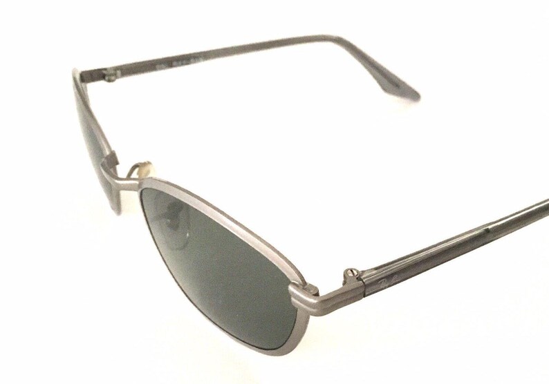 May include: Silver-toned metal sunglasses with dark gray lenses. The sunglasses have a thin frame and a slightly curved shape.