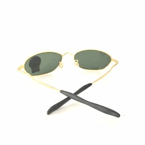 May include: Oval sunglasses with a gold frame, dark green lenses and black temple tips.