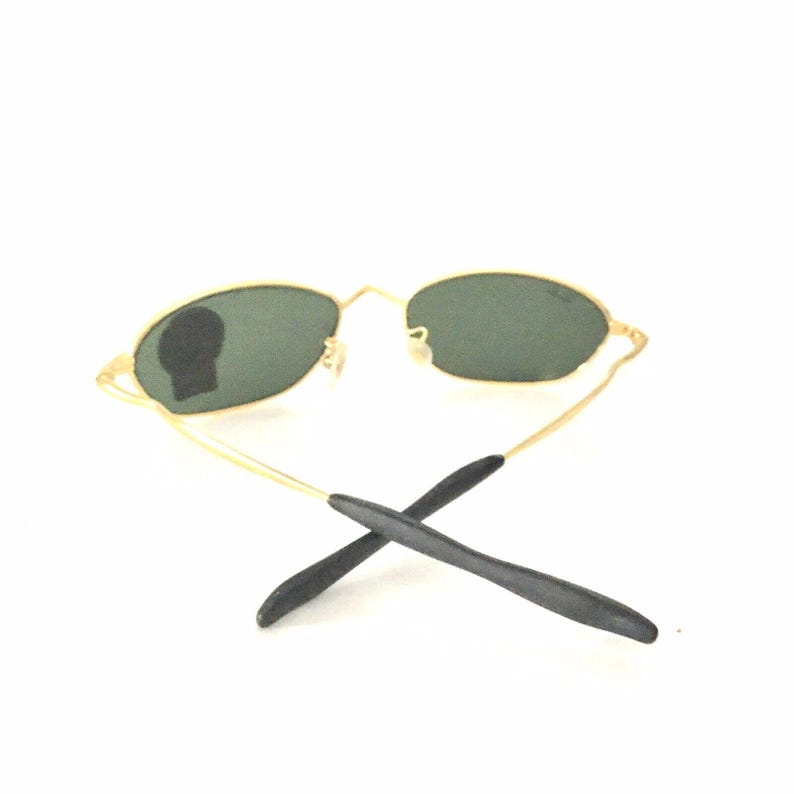 May include: Oval sunglasses with a gold frame, dark green lenses and black temple tips.