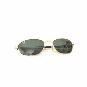 May include: Gold-framed sunglasses with dark green lenses. The sunglasses have a Ray-Ban logo on the left lens.