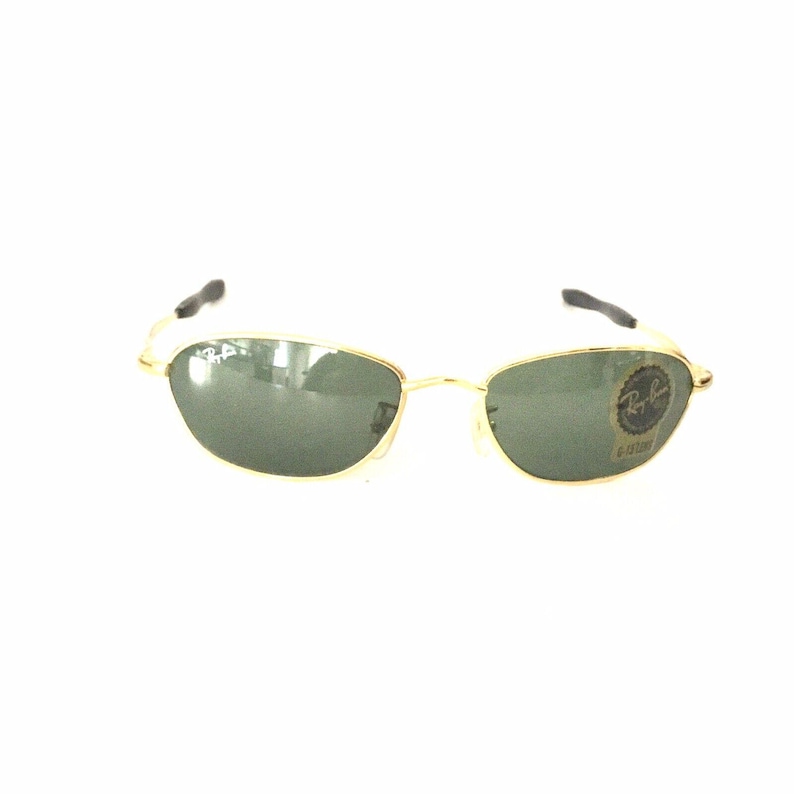 May include: Gold-framed sunglasses with green lenses. The sunglasses have a Ray-Ban logo on the right lens.